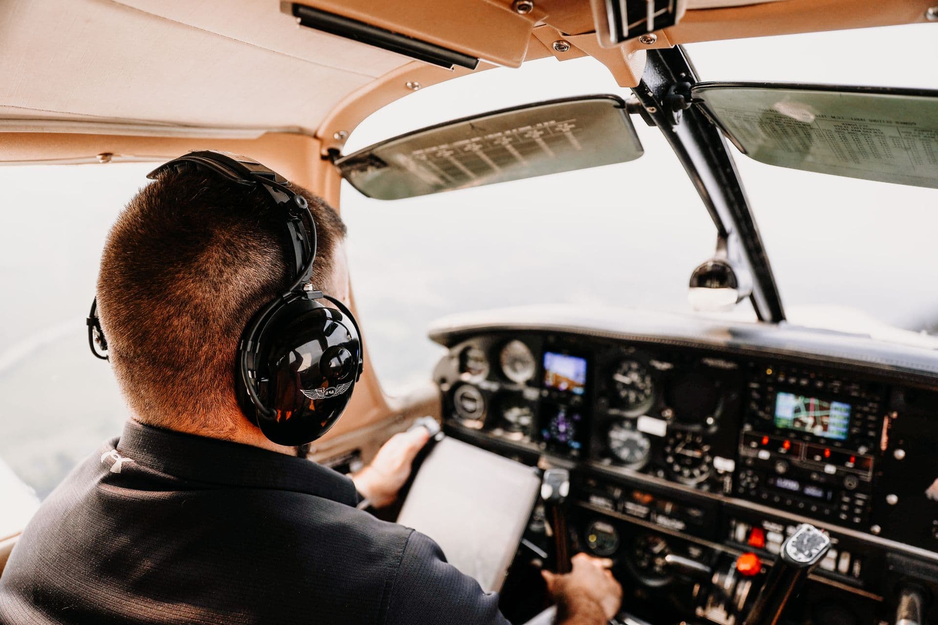 Un pilota con le cuffie, di spalle, ai comandi di un aereo da scuola